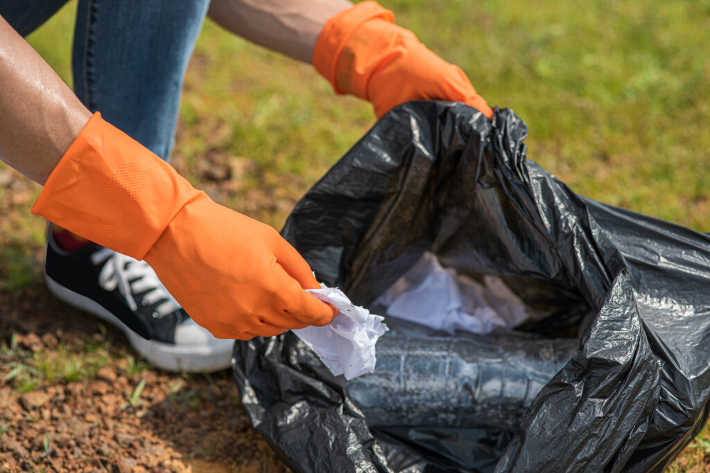 A man wearing orange gloves collecting garbage in a black bag.